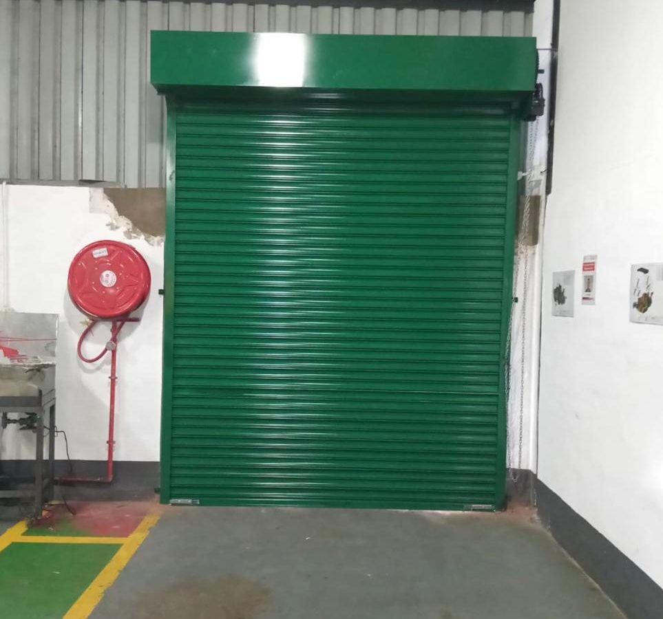 Green industrial roller shutter door installed next to a fire hose reel
